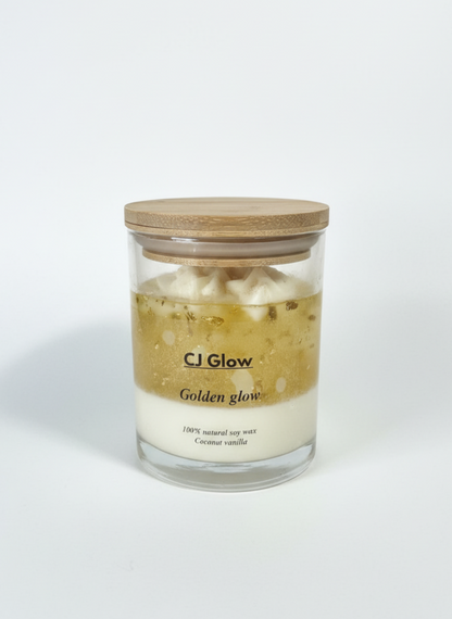 Glass candle with wooden lid labeled 'CJ Glow Golden glow' on a white background